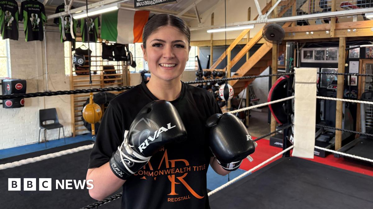 Megan Redstall raises her boxing gloves for the camera as she stands in the ring.