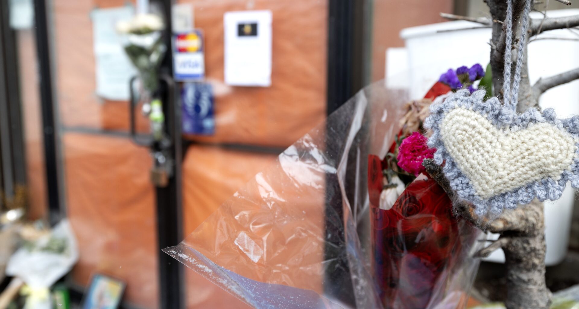 Flowers and other items are seen outside a locked storefront.