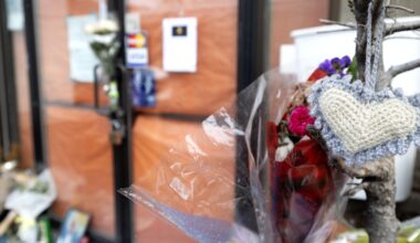 Flowers and other items are seen outside a locked storefront.