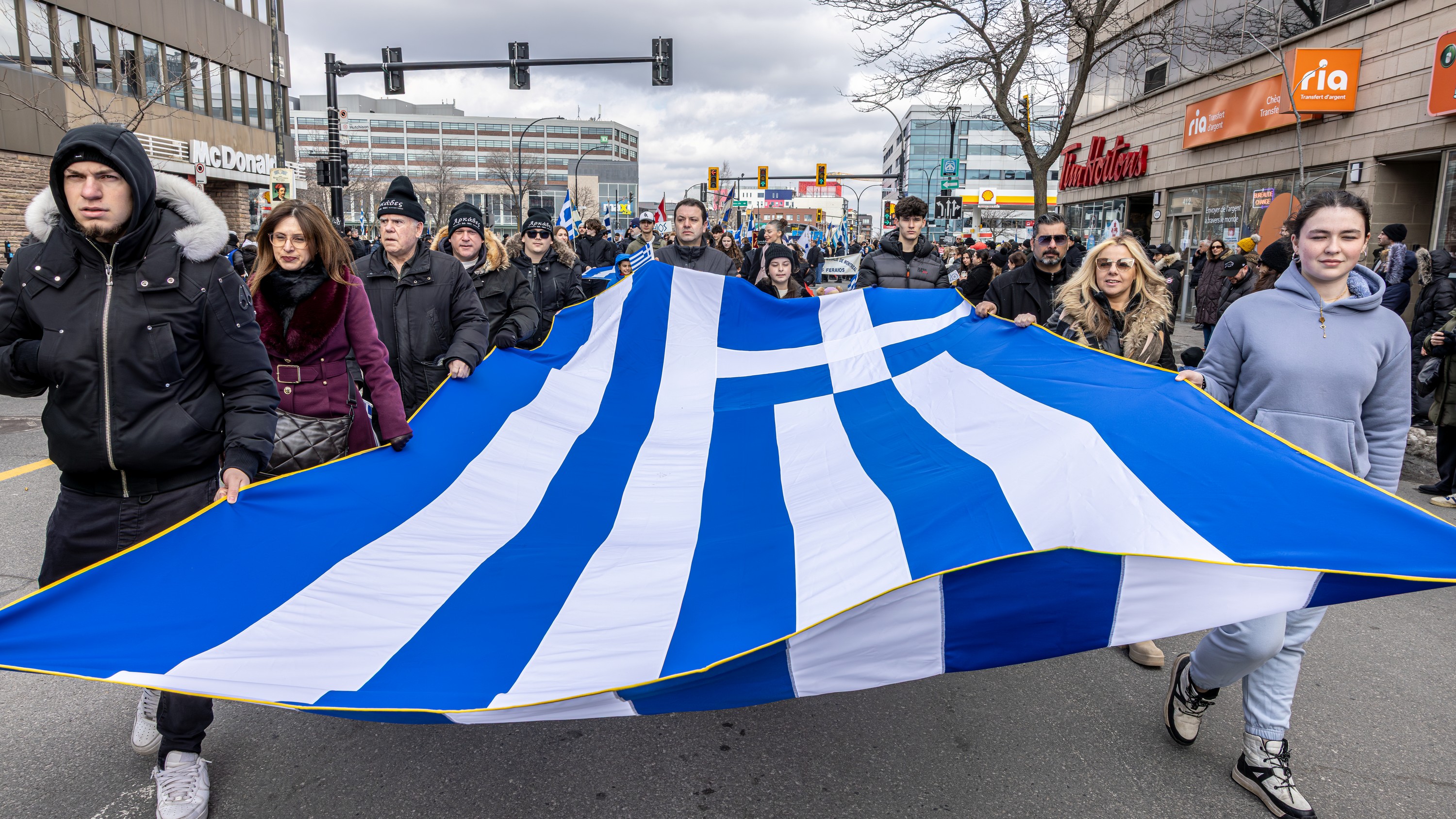 Parade participants carry a large Greek flag.