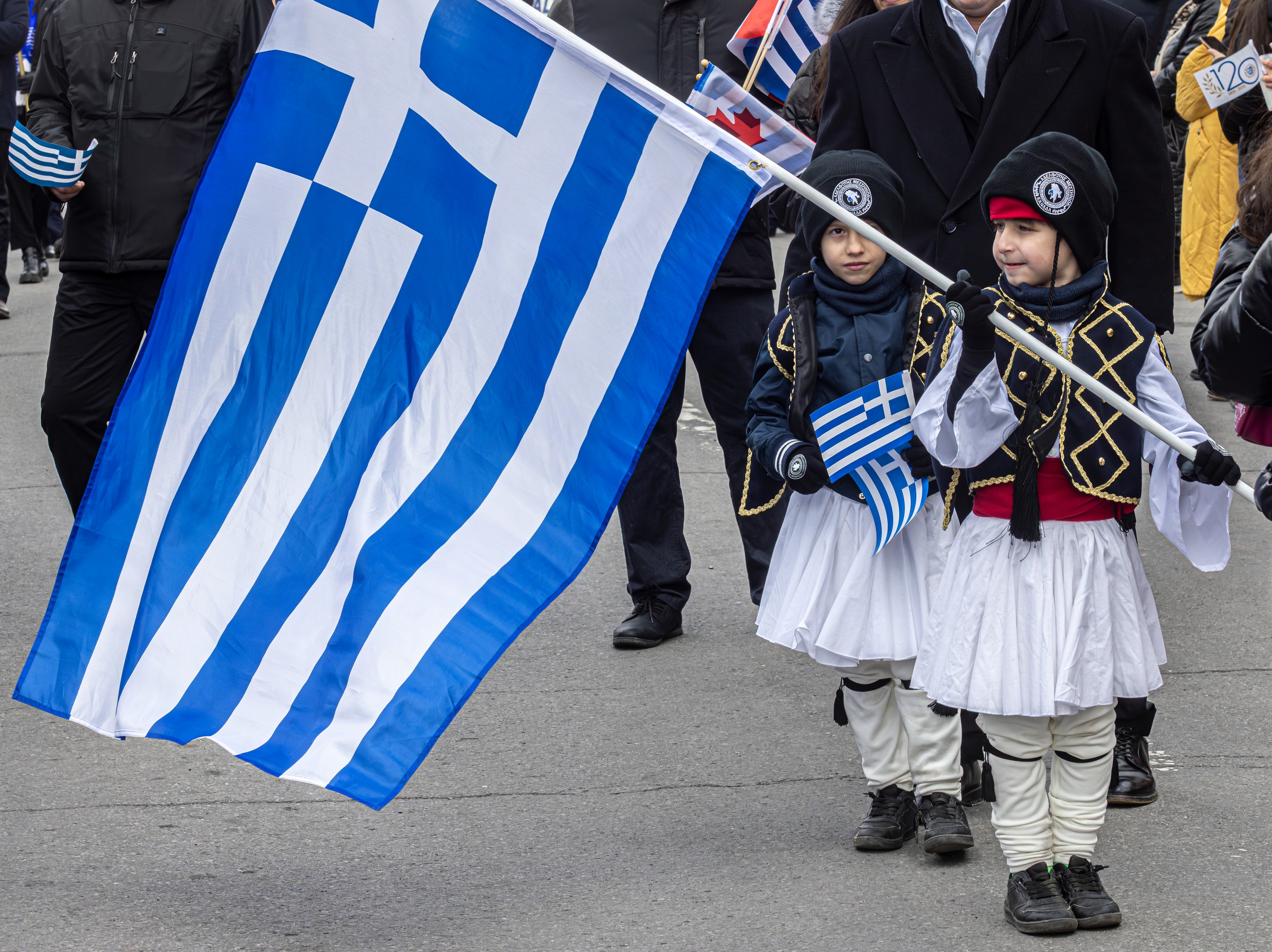A small child waves a Greek flag in a parade.
