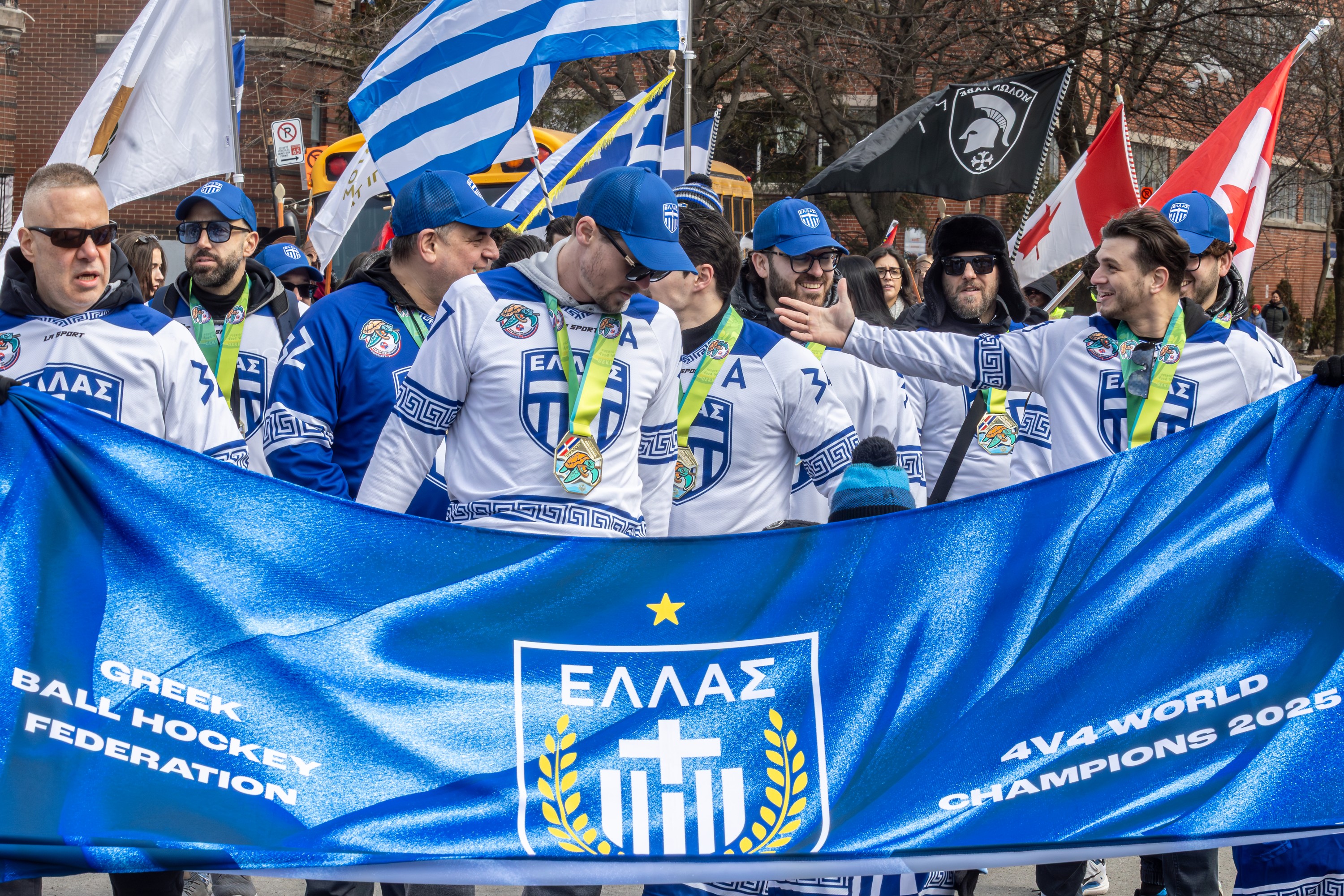 A group of men stand behind a parade banner that reads Greek Ball Hockey Federation.