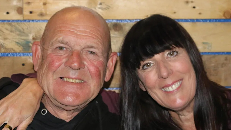 Tom and Julia smile as they pose together for a picture. Julia has her arm around his shoulder.