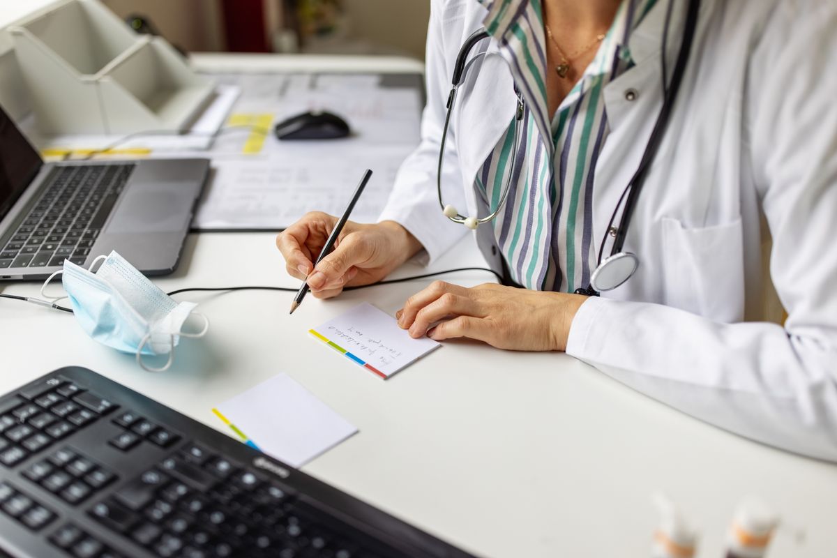 Close-up of a doctor preparing prescription while consulting a patient over video conference. Female doctor making notes while talking with patient on video call.