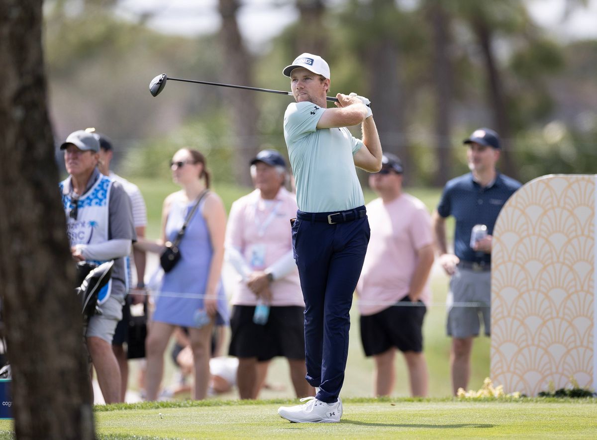 An individual engaged in a golf swing on a golf course, with a crowd of spectators in the background, observing the action.