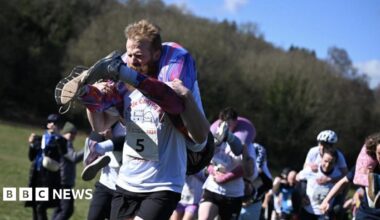 A group of people carrying others on their shoulders. Some are giving the person they are carrying a piggy back, others are carrying with the person's feet in front of them, and them hanging down their back.