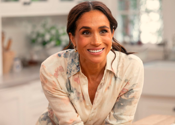 Meghan Markle smiling in a light patterned shirt in a bright, softly lit kitchen setting for Netflix brand coverage.