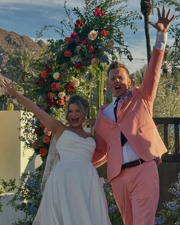 JoJo Siwa and Chris Hughes celebrating their wedding outdoors with floral arch and joyful expressions after walking down the aisle.