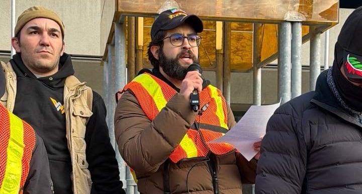 A man in a safety vest speaks into a microphone. 