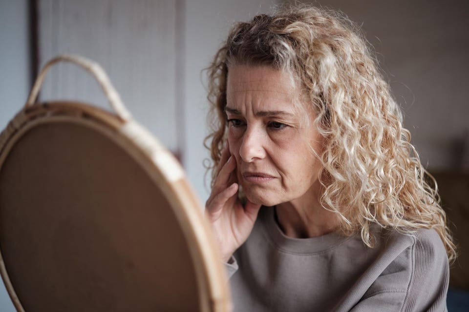 Sad middle-aged woman looking in mirror