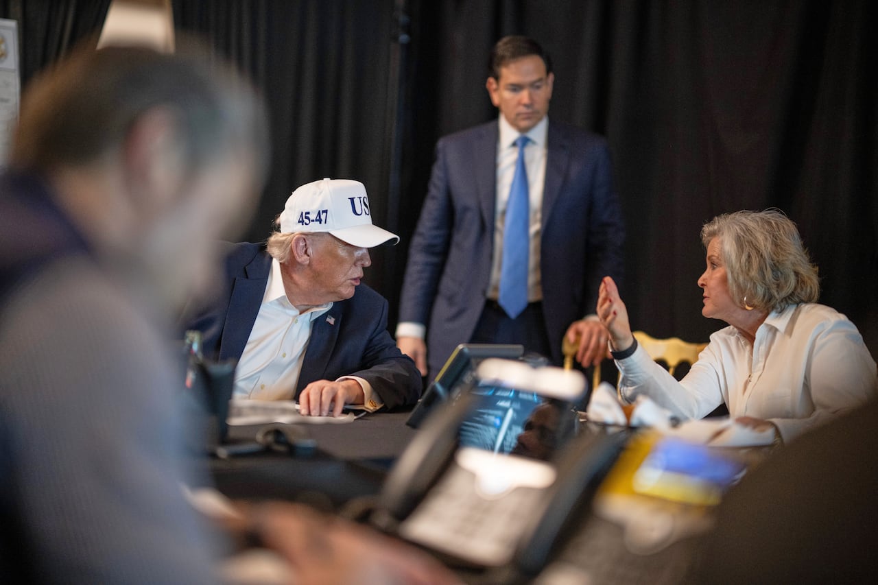 Donald Trump wears a white hat while speaking with advisers.
