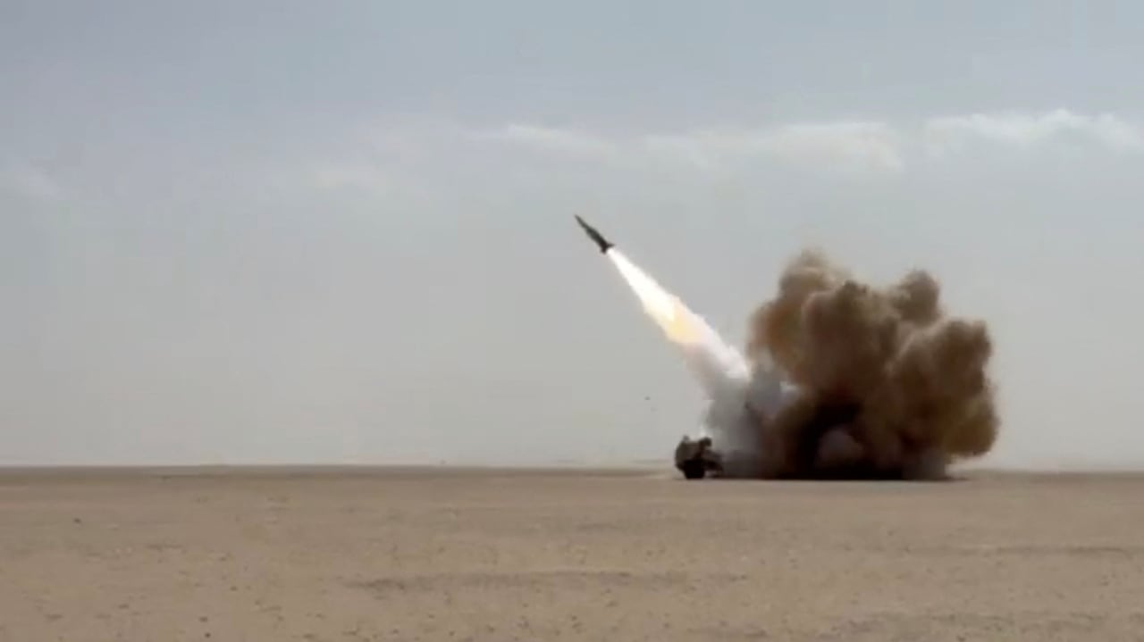A missile flies up from the ground with a flame and a large plume of smoke behind it.