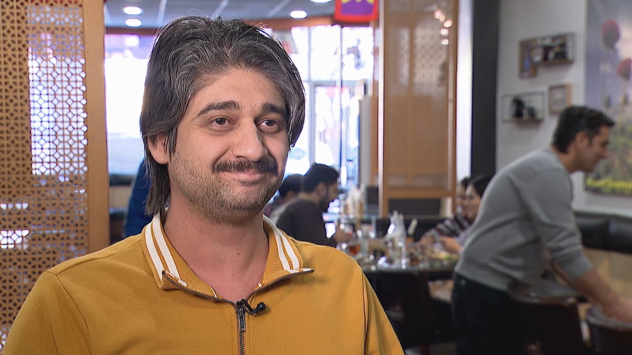A man wearing a yellow polo stands in a busy restaurant.