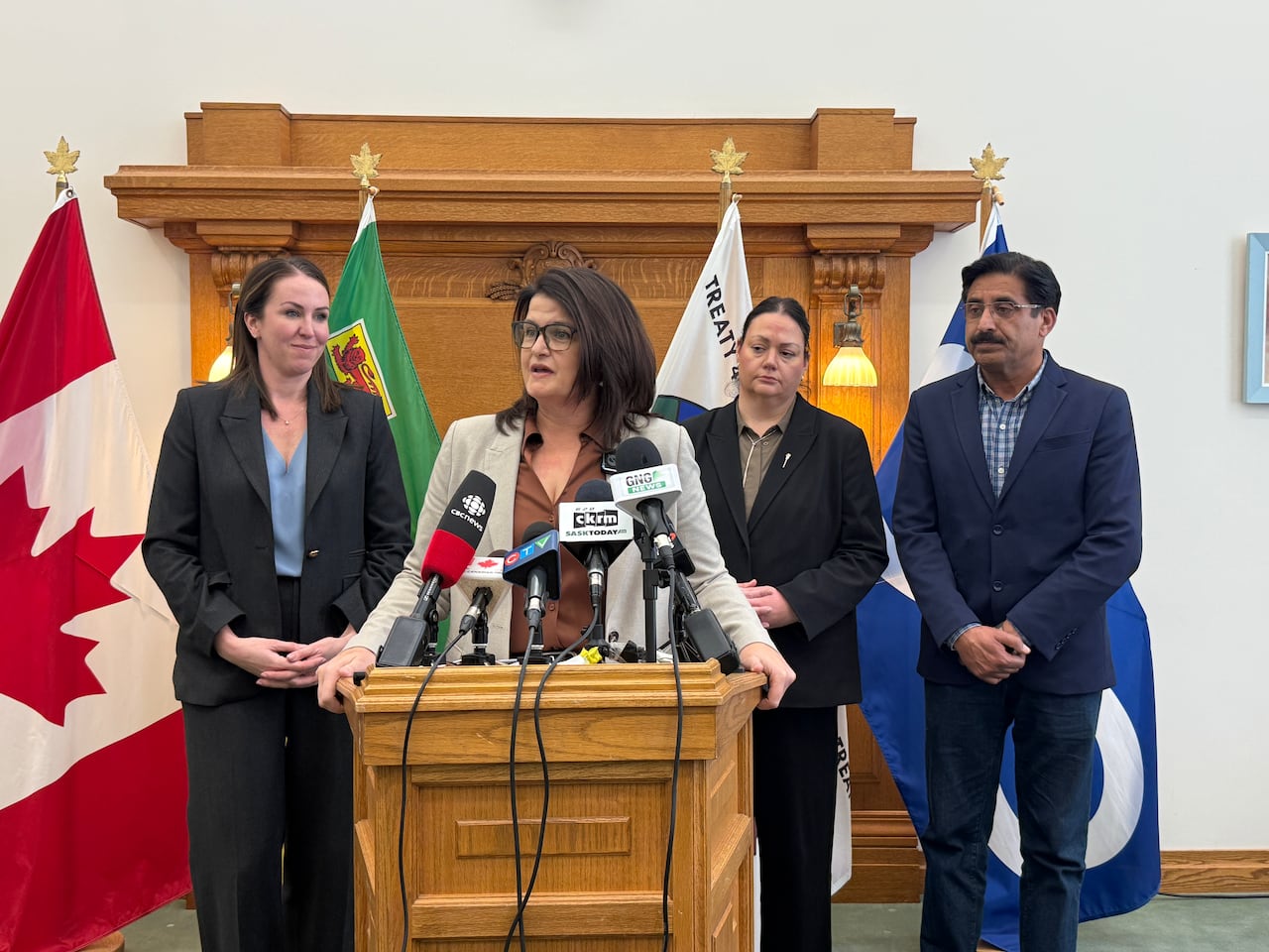 A woman stands at a wooden lectern. Two women and a man stand behind her.