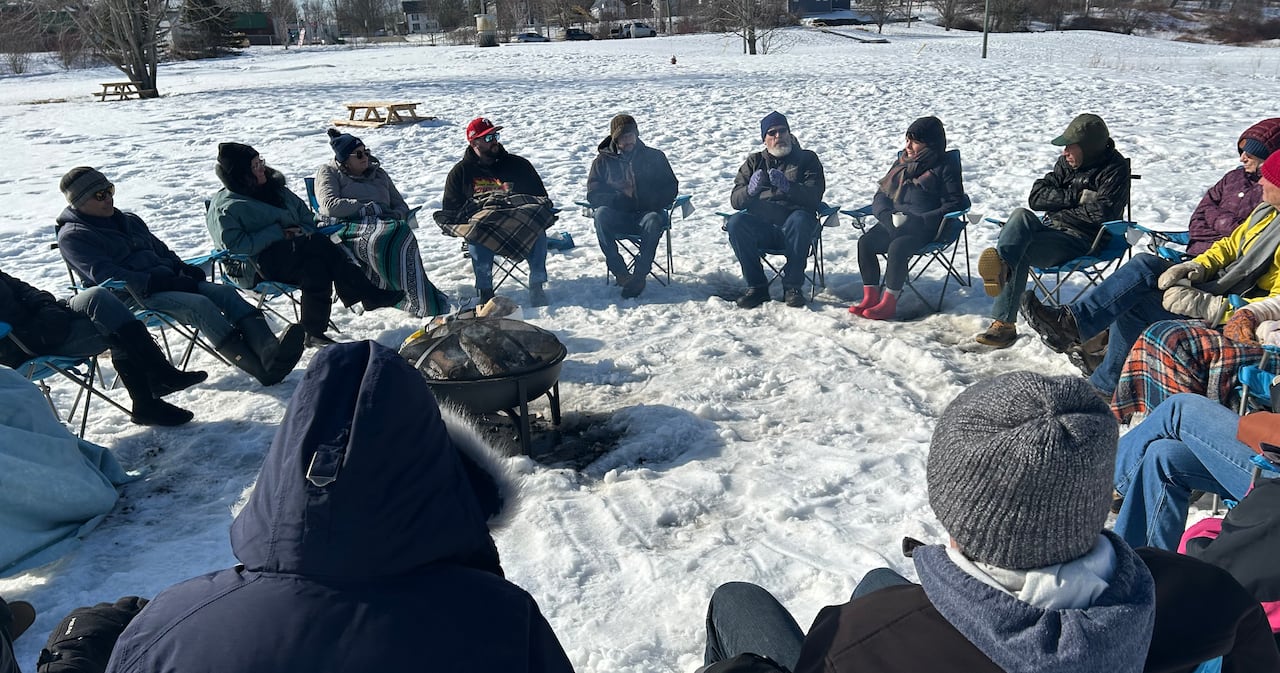 People are sitting in a circle around a fire outside on a snowy day.