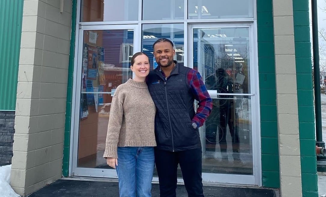 A woman and a man stand in front of a store, both smiling proudly.