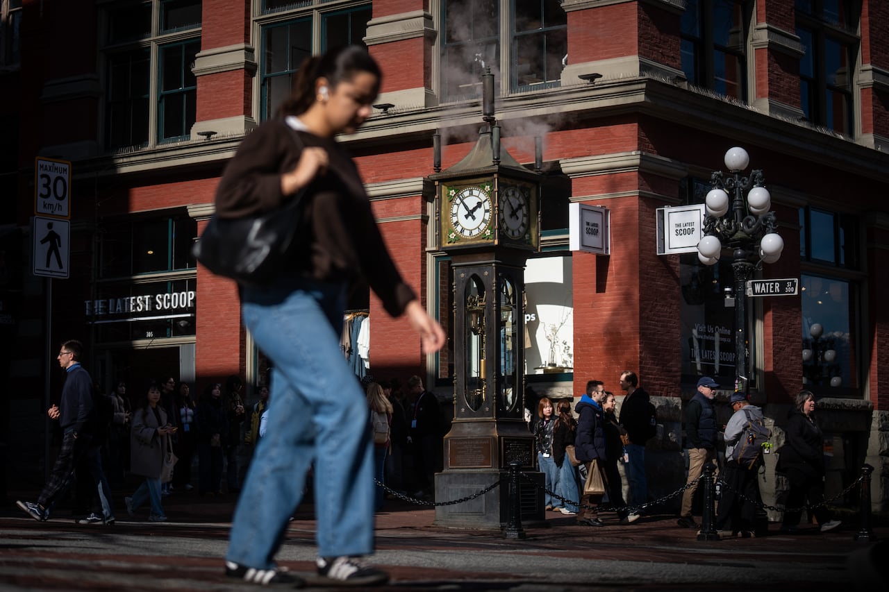 A woman walks across the street from the Gastown steam clock, which has steam rising from it