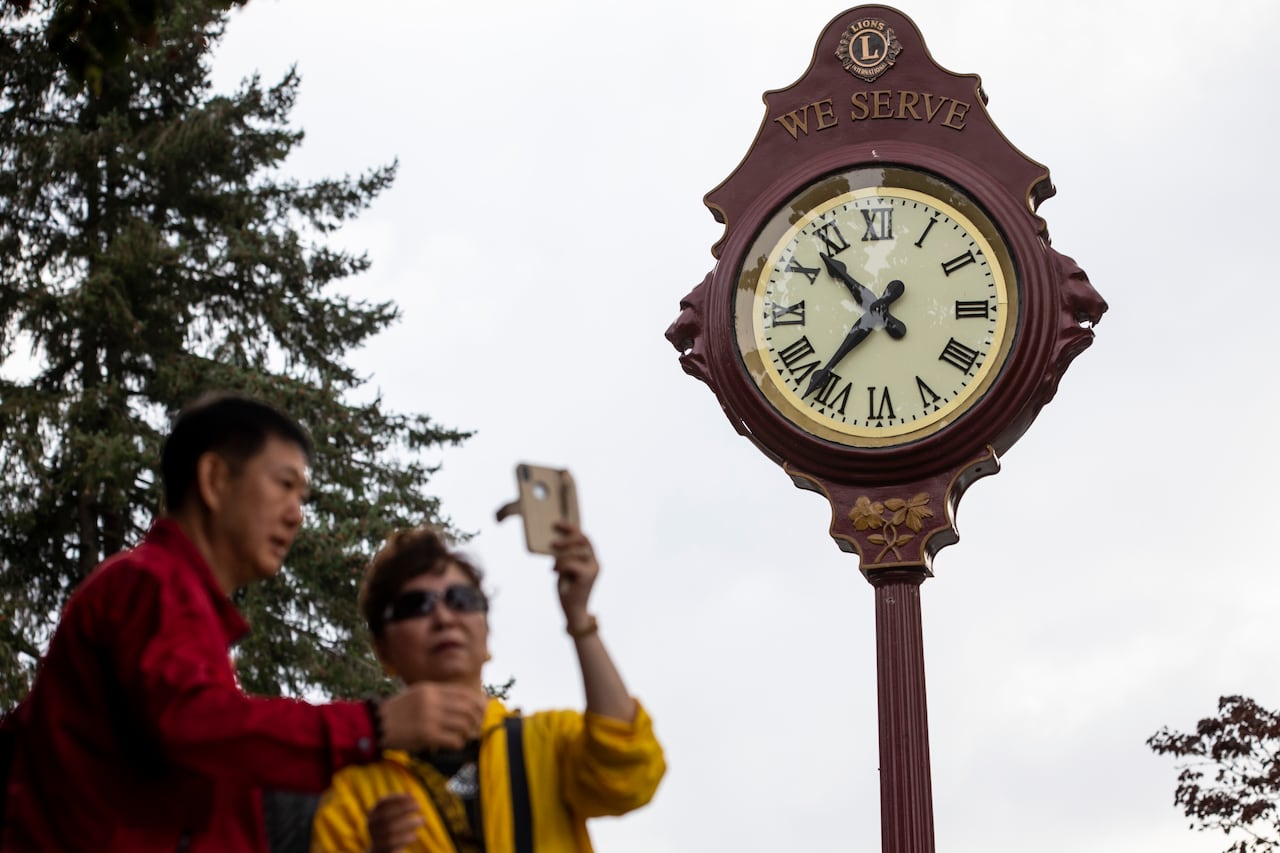 Two people take a selfie near a historic-looking clock with Roman numerals.