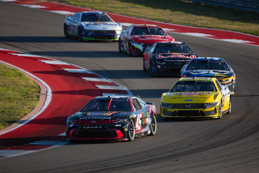 NASCAR cars race around a corner at a racetrack.