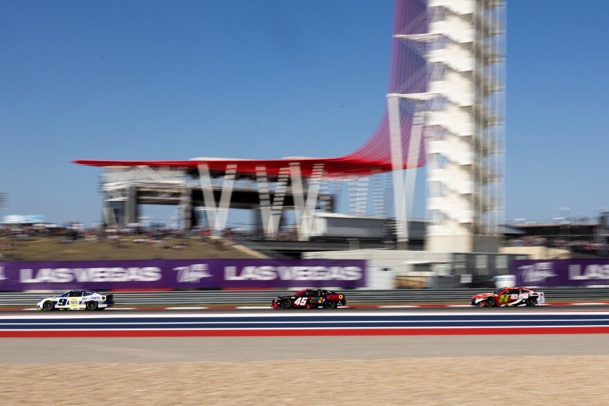 Cars race along a track with a large tower in the background. 