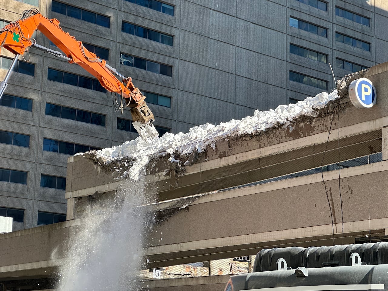 Snow falls from the building as a construction machine works on the parking garage later on Feb. 26, 2025.
