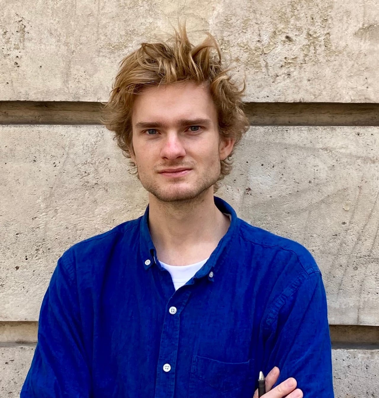 A man in a blue shirt poses for a photo in front of a building exterior wall