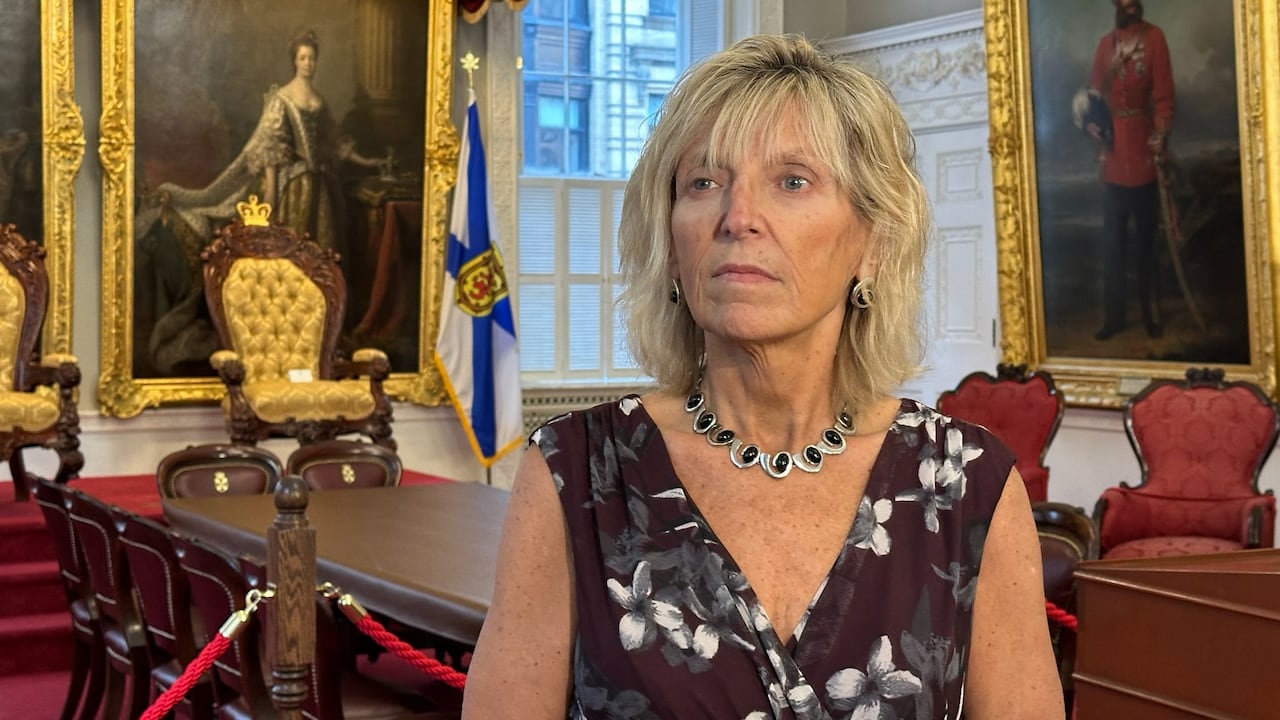 A woman stands in a room decorated with paintings and a red carpet.