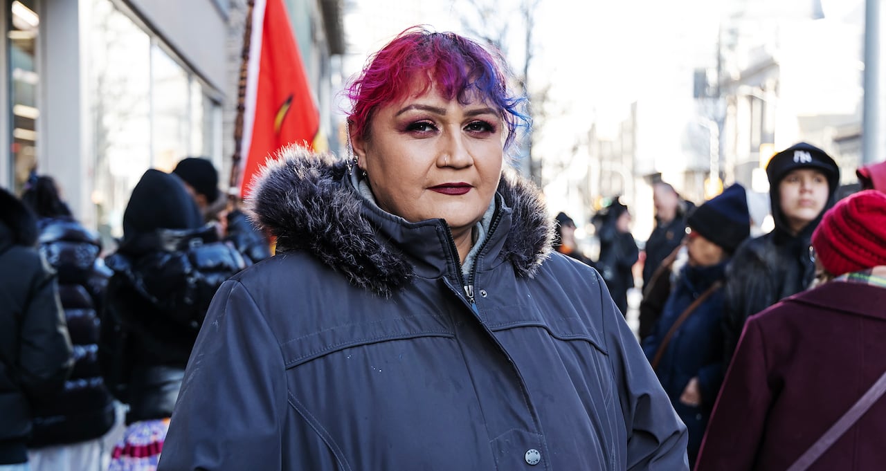 woman with purple and blue hair wears a blue winter jacket and stands in a crowd on a city street
