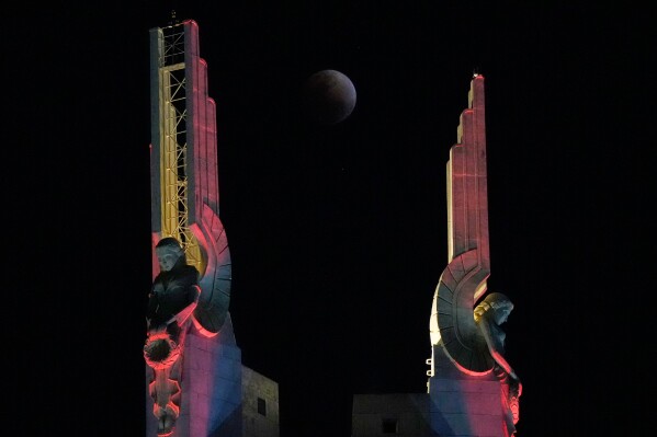 A total lunar eclipse is seen through statues at the Quezon Memorial Shrine in Quezon City, Philippines, Tuesday, March 3, 2026. (AP Photo/Aaron Favila)