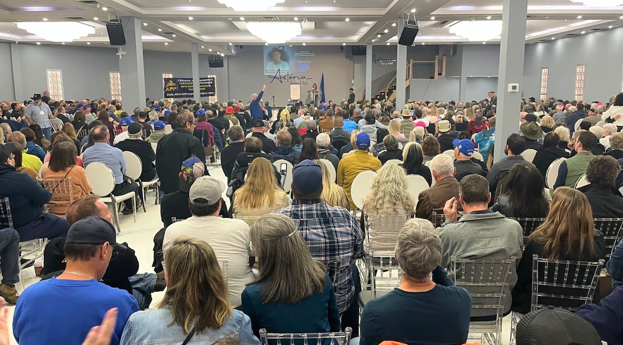 A large crowd of people face the front of a banquet hall.