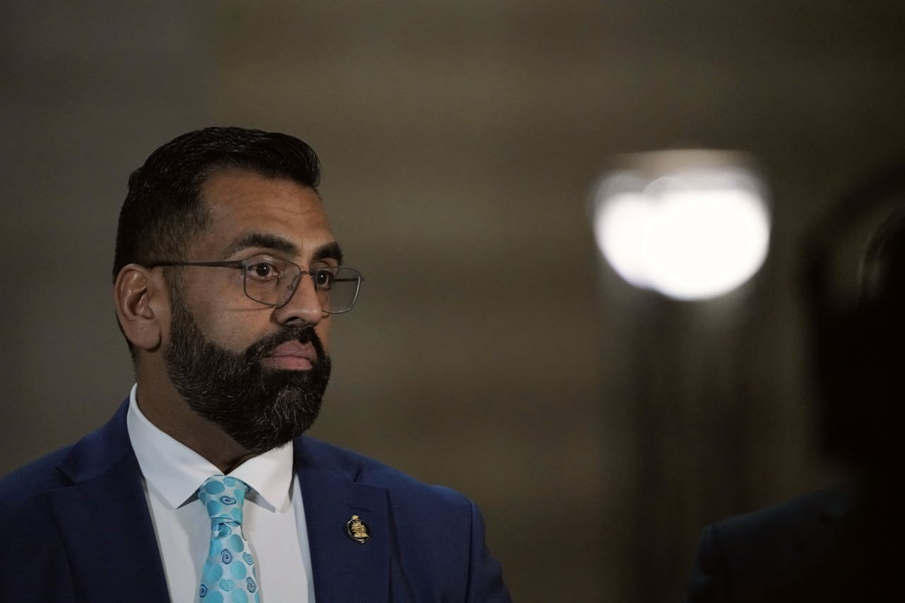 A man in a blue suit and light blue tie speaks with media.