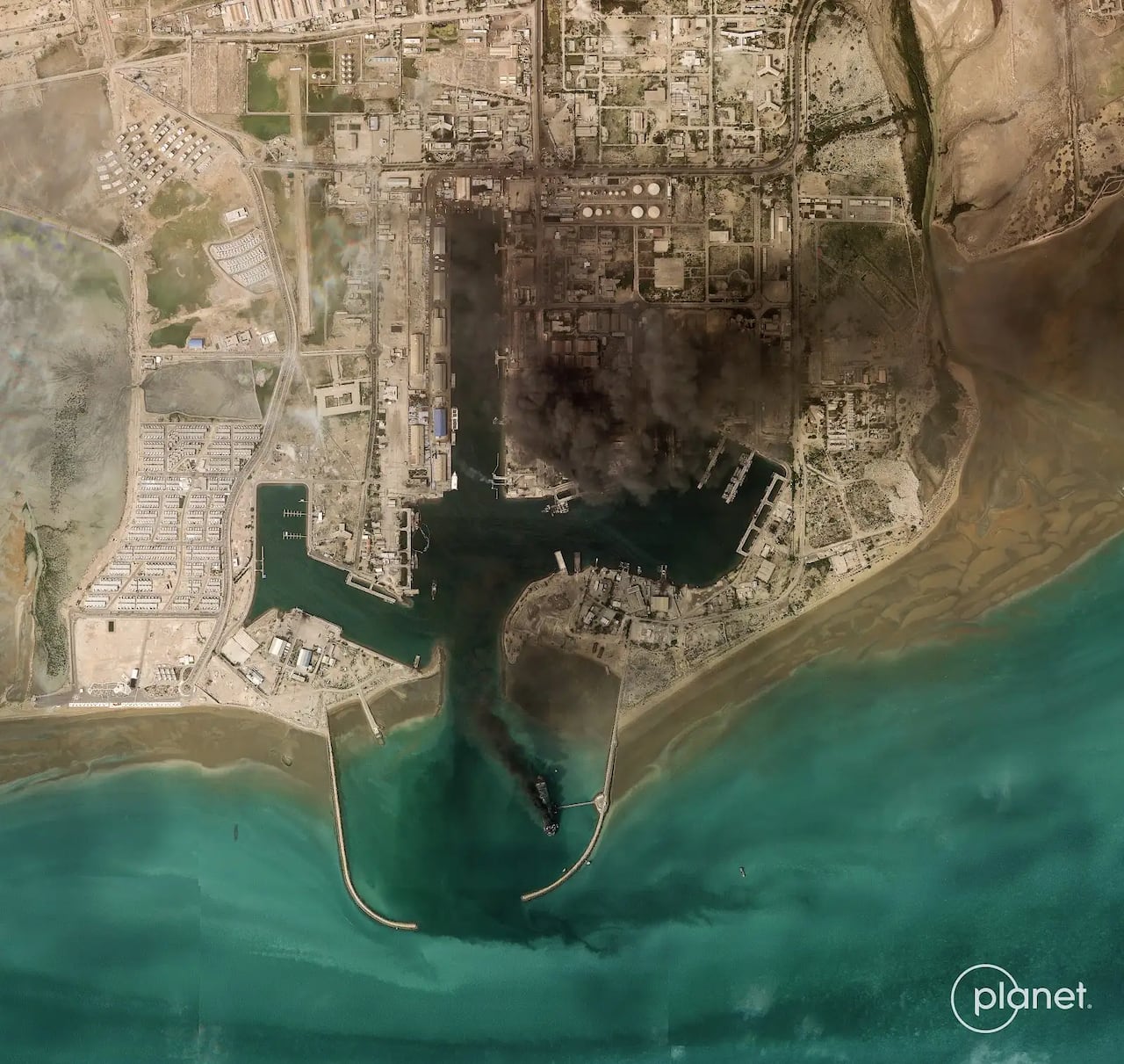 A satellite image of a militayr harbour with smoke rising over it. 