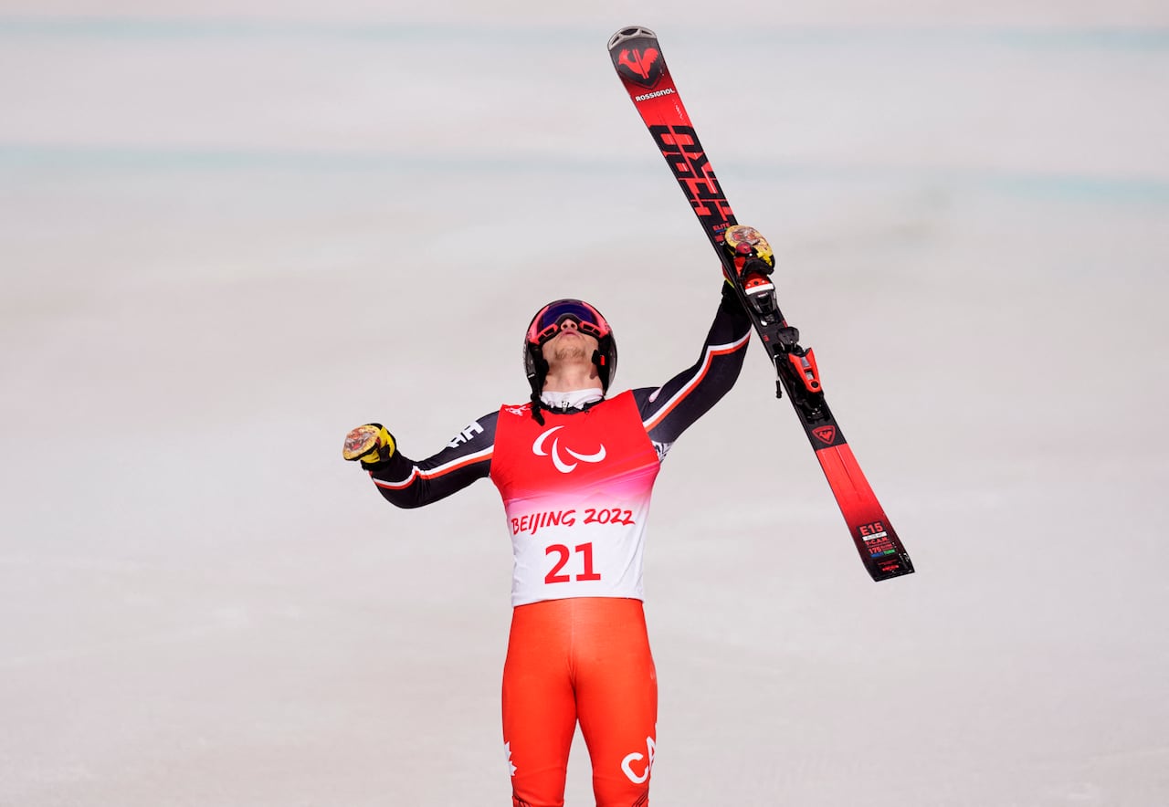 A downhill skier lifts one ski in celebration after finishing a race.