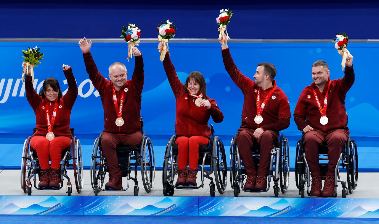 A team of wheelchair curlers in red outfits celebrate a Paralympic medal.