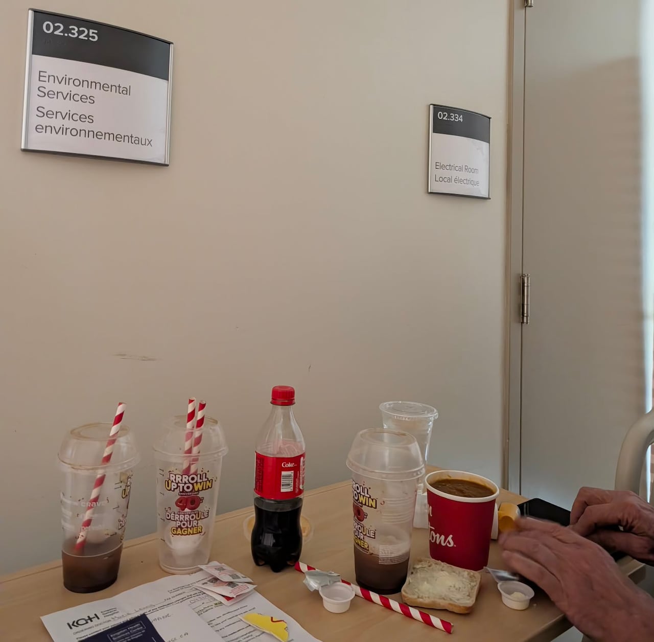 A table covered in drink bottles and cups next to signs on the wall that indicate an electrical room.