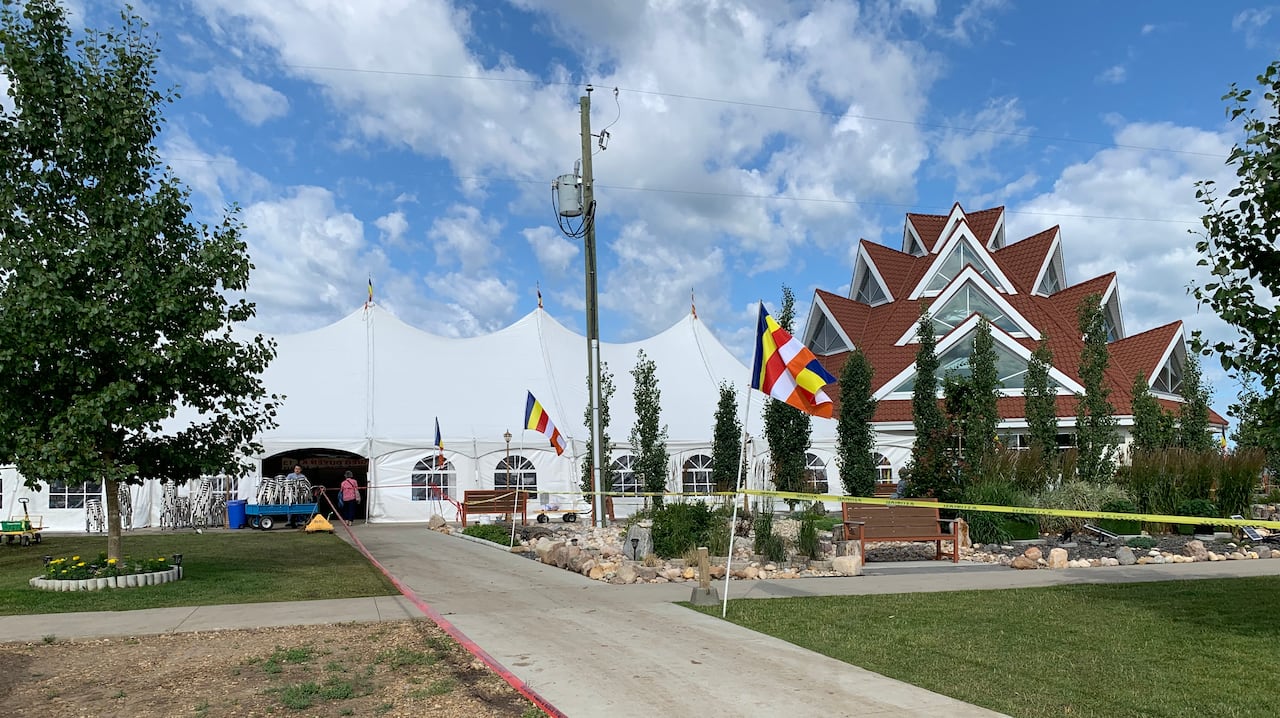 Yellow caution tape blocks access to a building featuring a burgundy roof with many peaks and windows and a large while event tent.