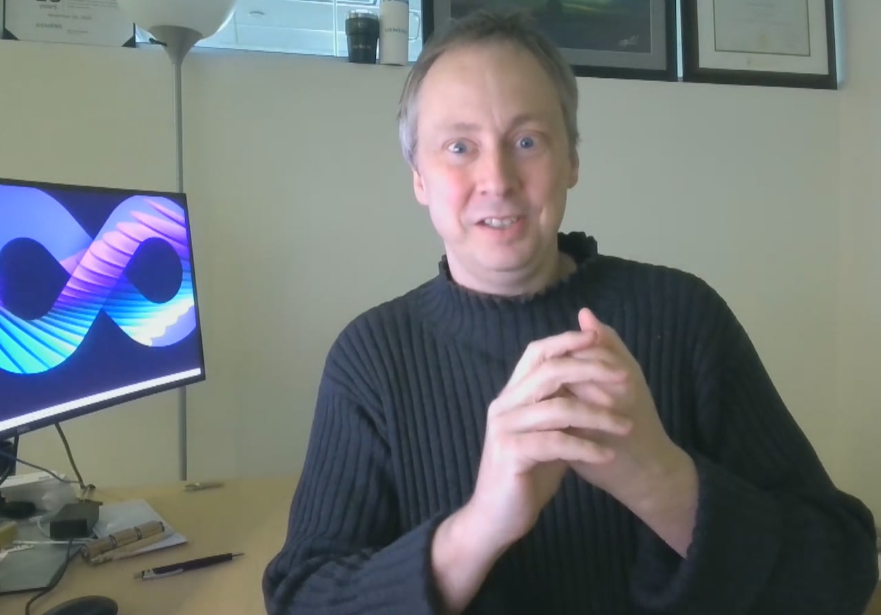 A man in a turtleneck sitting next to a computer.