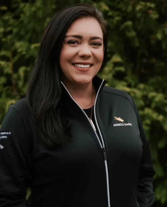 A woman with dark hair and a sweater smiles brightly at the camera