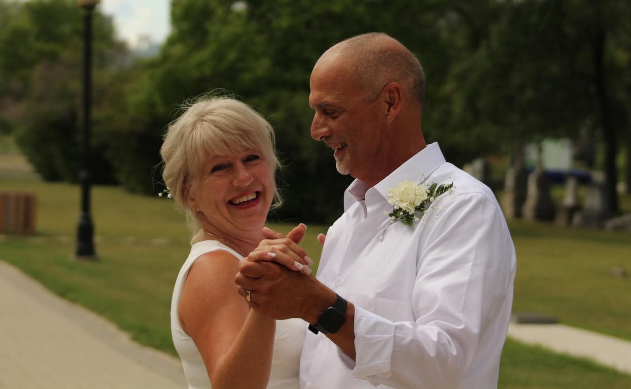 A man and a woman dressed in white hold hands together.