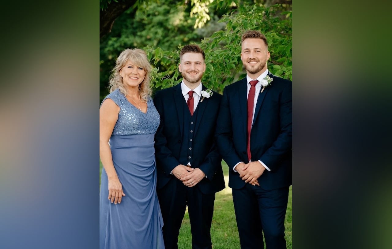 A woman wearing a blue dress stands besides two men wearing a smoking and red tie.