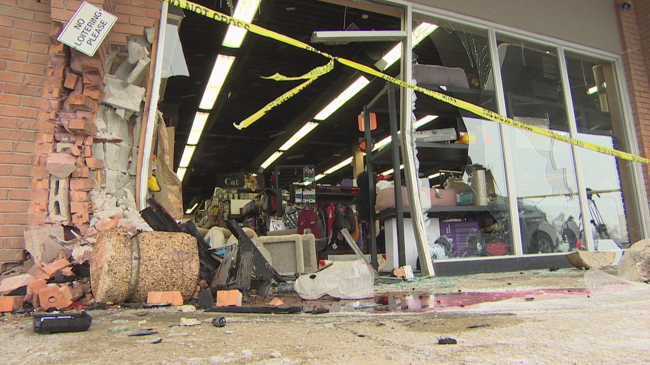 Debris, including bricks, glass and car parts, lay scattered on the ground. The glass front of a store is shattered and missing.