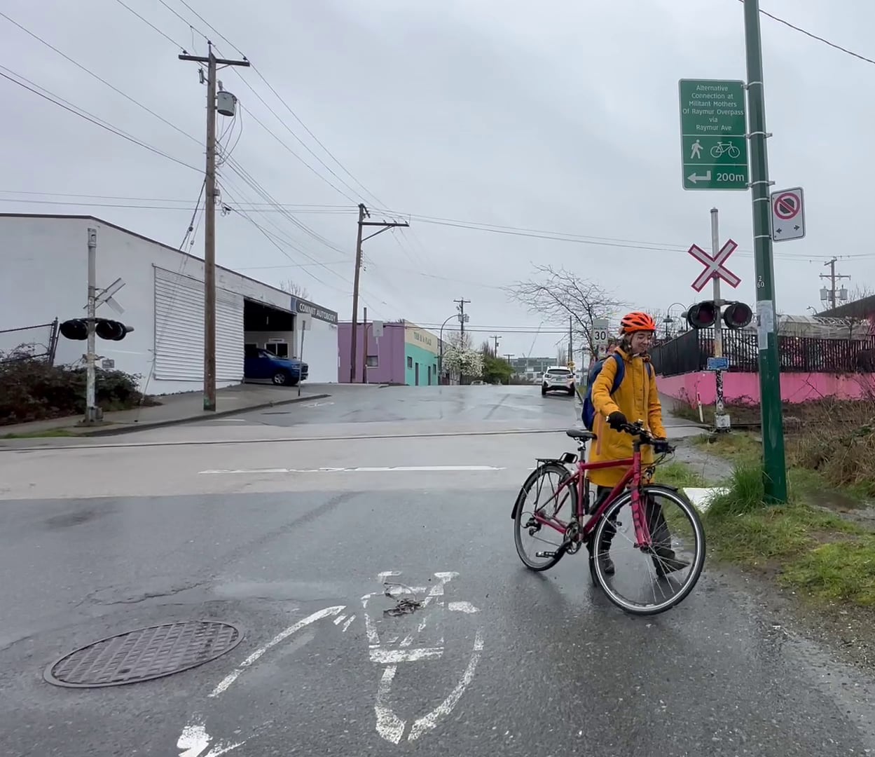 A woman wheels her bike past a railway crossing on a rainy day.