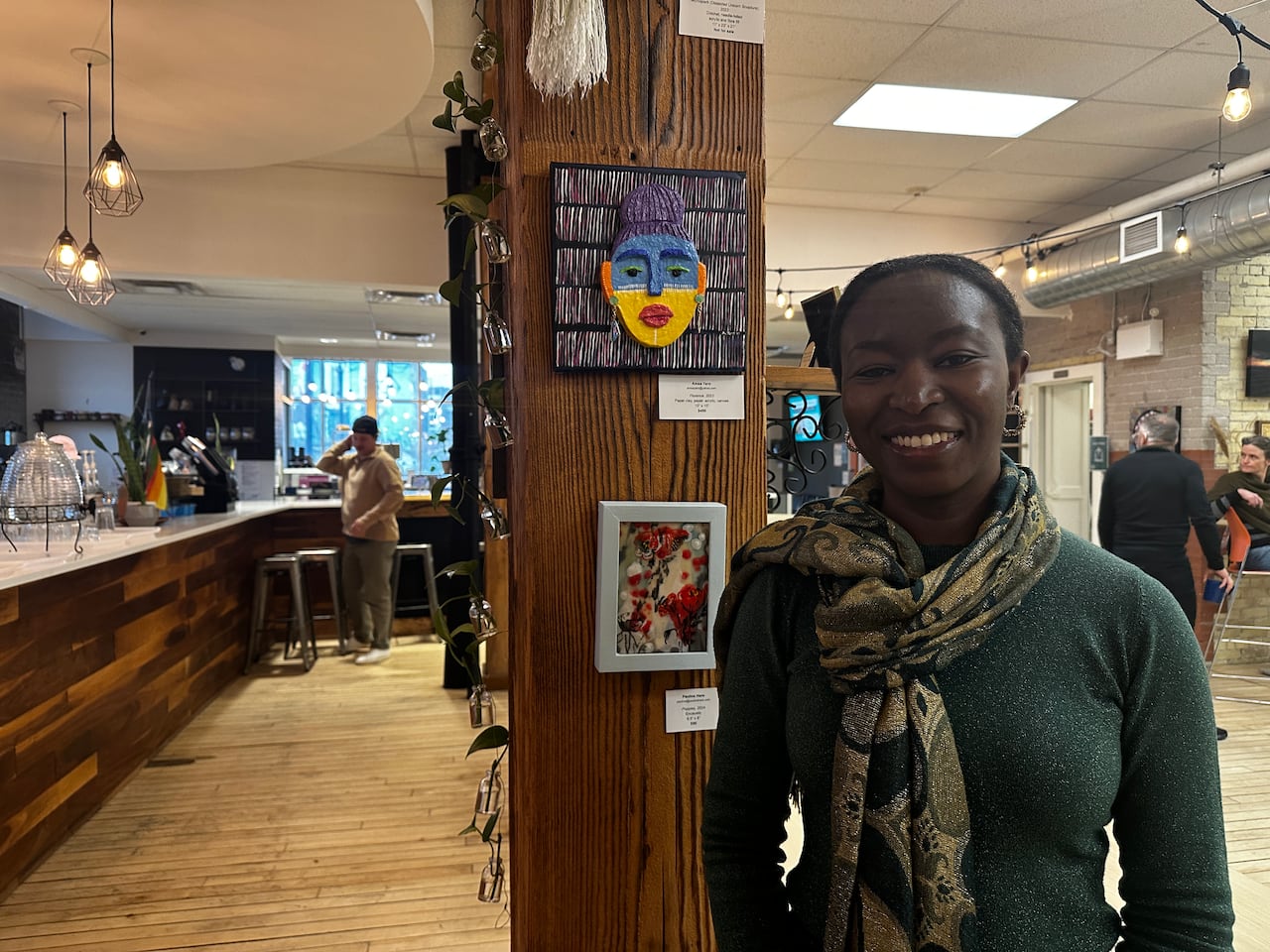 Woman stands next to colourful art piece made of recycled materials. 