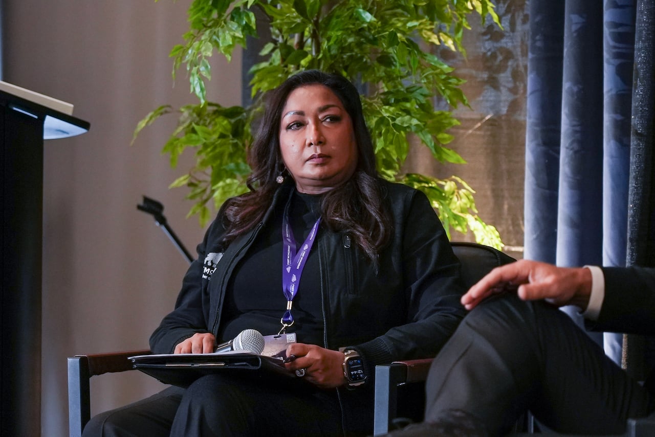 A woman holding a microphone in her hand sits on a chair.