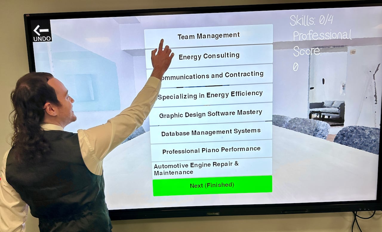 A student in a business attire stand pointing to words on a screen of a big screen tv.