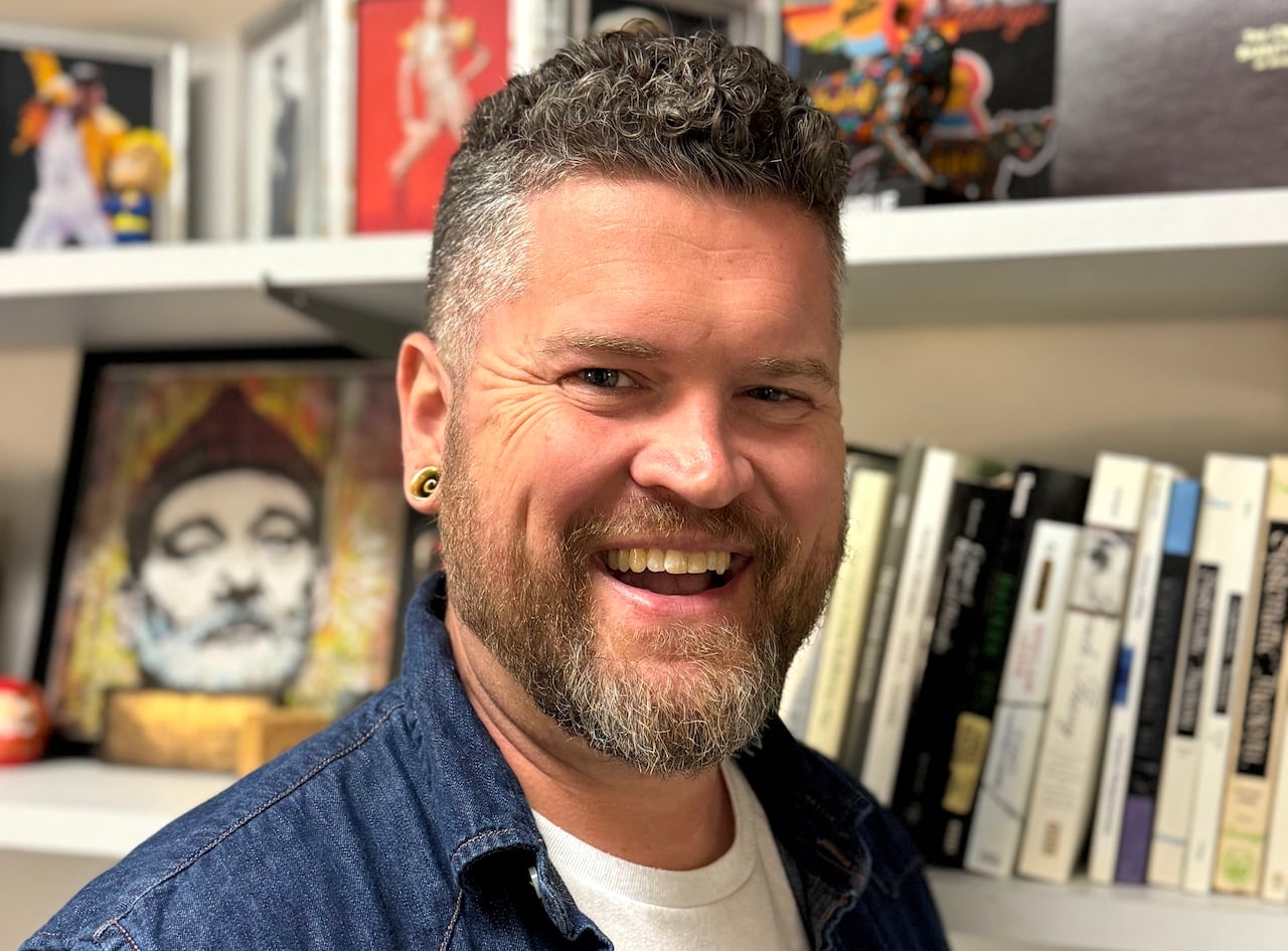 A smiling man is shown in front of a bookshelf.