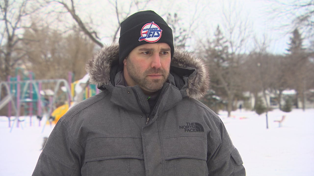 Man with short beard wears a grey winter jacket and a black Winnipeg Jets hat outside in the snow