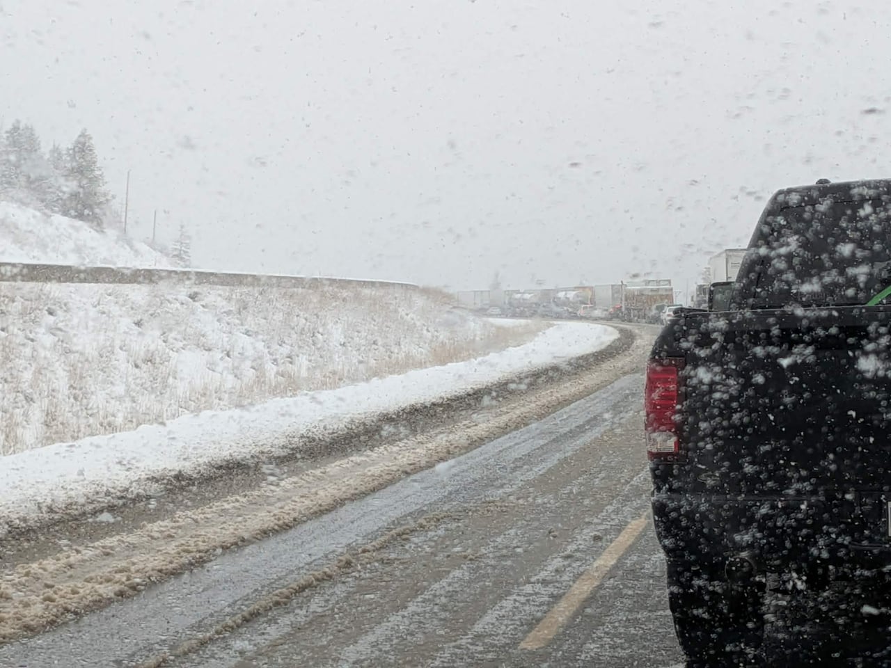 Heavy snow falls over a line of stopped vehicles on a highway.