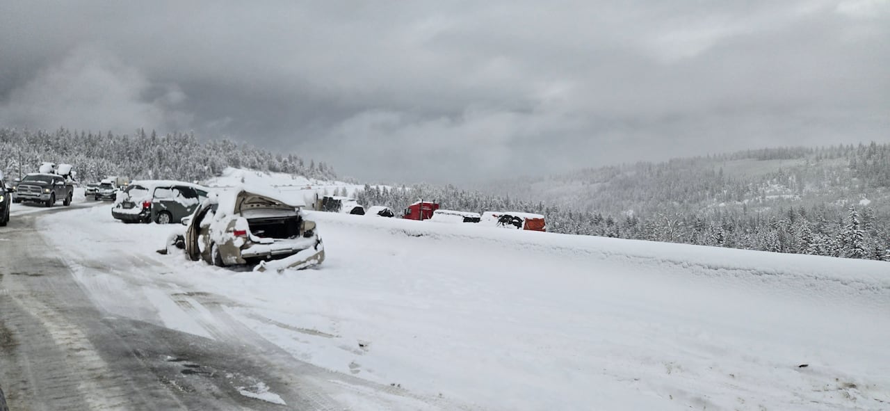 A snow-covered vehicle sits damaged on the side of a highway following a crash.