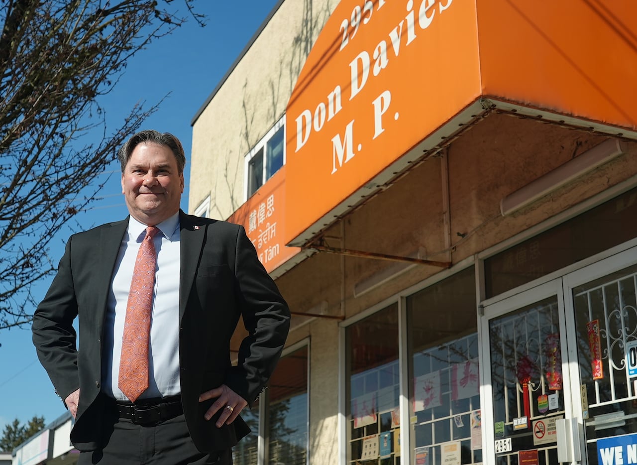 Man in suit with arms on his hips standing in front of a ground-floor office